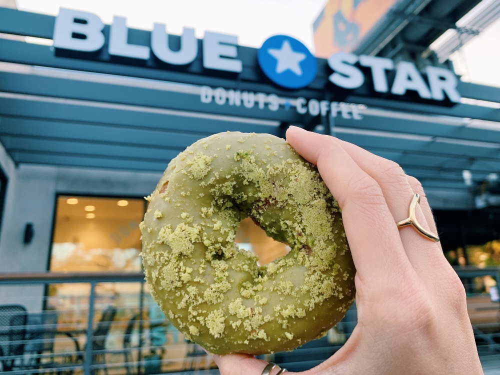 Blue start matcha donut held up with the restaurant in the background