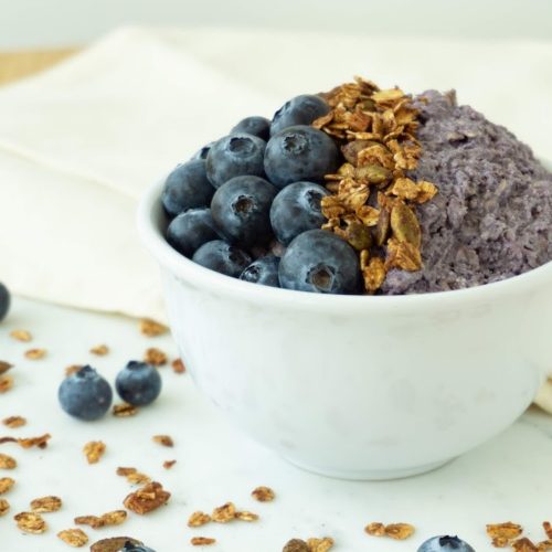 Blueberry cheesecake overnight oats on a white cloth topped with fresh blueberries and granola.