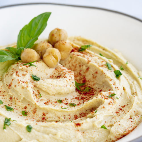 Classic hummus topped with chickpeas, basil, and paprika in a white bowl
