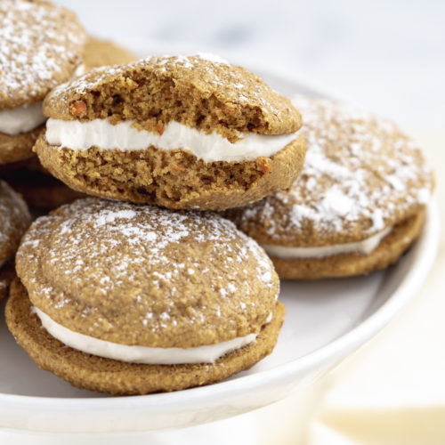 Four vegan Whoopie pies on a white dish with a cream cloth in the background.