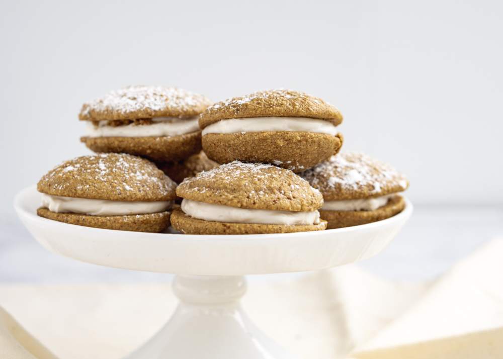 Six Whoopie pies on a white ceramic cake stand with a cream cloth in the background.