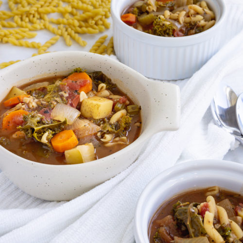 Easy minestrone soup in ceramic bowls with spoons and dry pasta in the background.