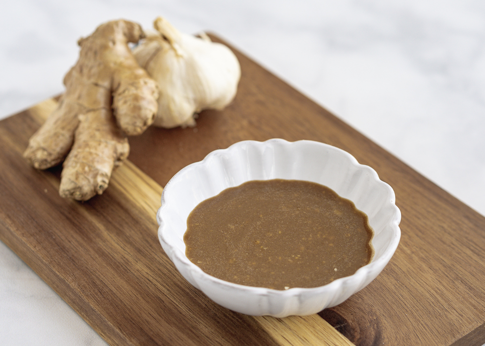 Miso Ginger Dressing in a white bowl with fresh ginger on a wood cutting board.