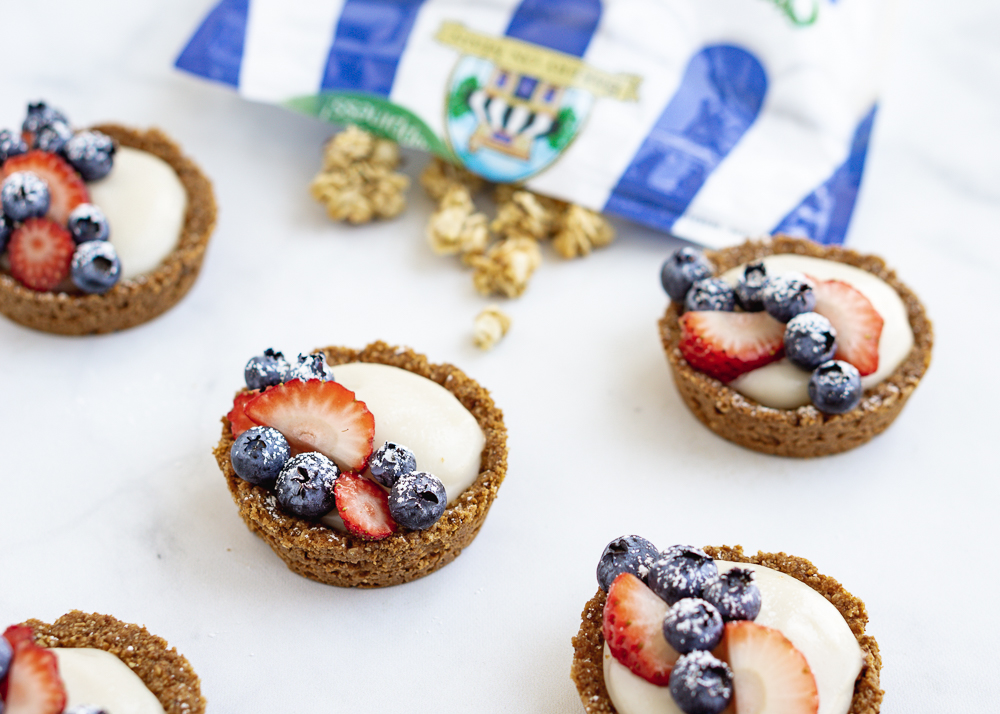 Five fruit tarts on a white background with Bakery On Main oats behind them.