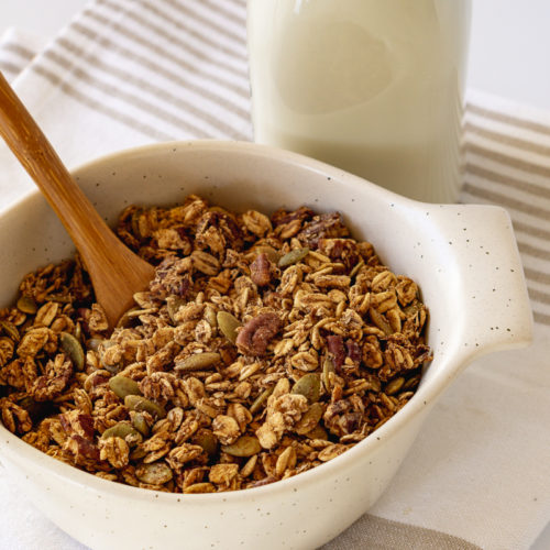 A bowl of chai spiced granola with a bottle of almond milk behind it