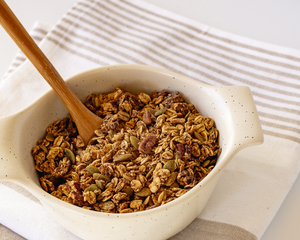 Bowl of chai spiced granola with a spoon on a cloth