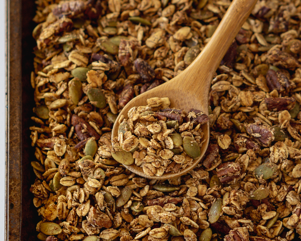 Chai spiced granola on a baking sheet lifted by a spoon