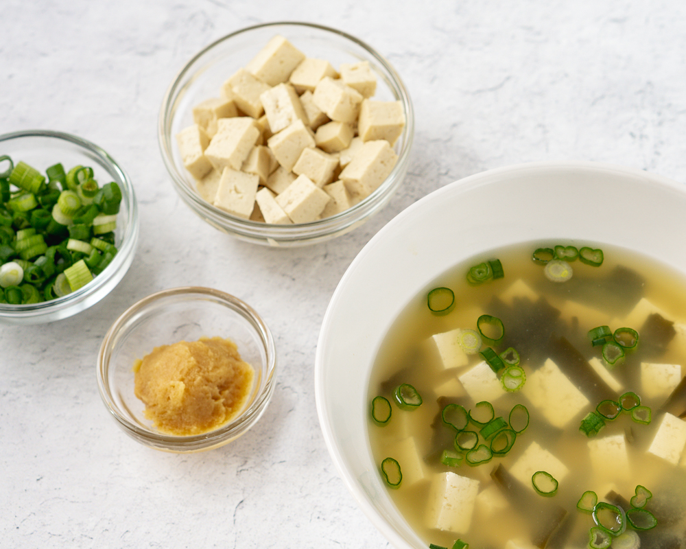 Bowl of homemade miso soup along with bowls of diced tofu, miso paste, and sliced green onions